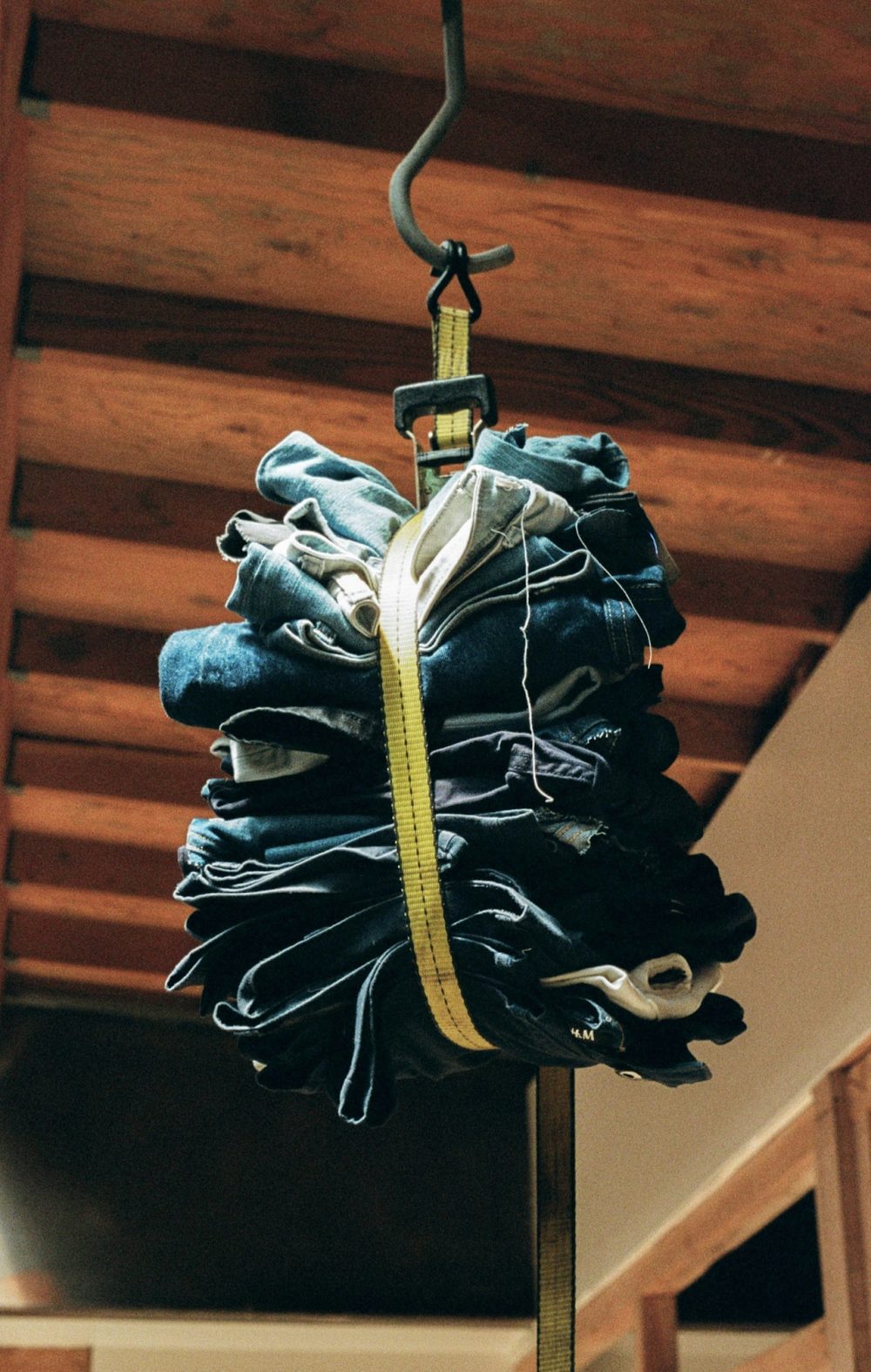 Image of a stack of denim jeans bundled together with a thick strap, hanging from the ceiling.